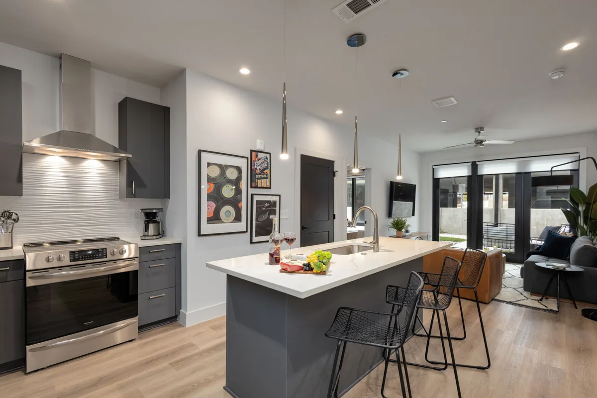 A bright, contemporary kitchen featuring a spacious island with bar stools, glossy stainless steel appliances, and modern artwork on the walls. Natural light fills the space, highlighting the clean countertops and inviting layout ideal for both meal prep and socializing.
