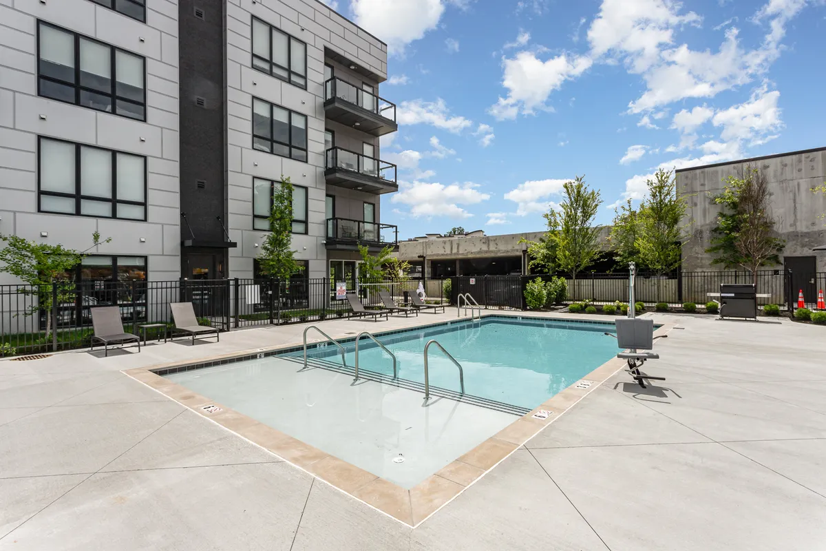 A sunny outdoor view of a resort-style swimming pool surrounded by lounge chairs and balconies, set amidst lush greenery, offering an inviting spot for relaxation and socializing between adventures.