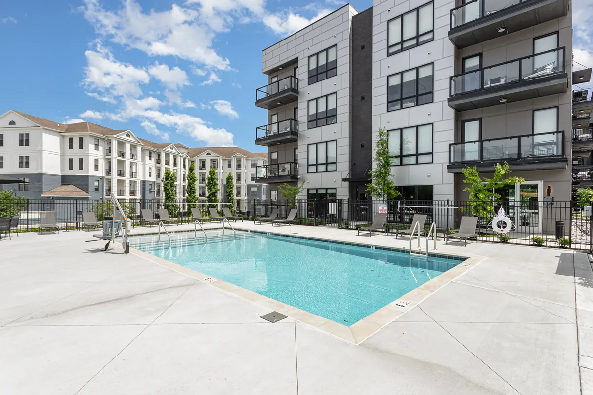 A sparkling swimming pool surrounded by sun loungers and balconies of the apartment complex. Lush landscaped greenery frames the pool, and soft sunset lighting adds a resort-like ambiance. The scene suggests both relaxation and the opportunity for social gatherings.