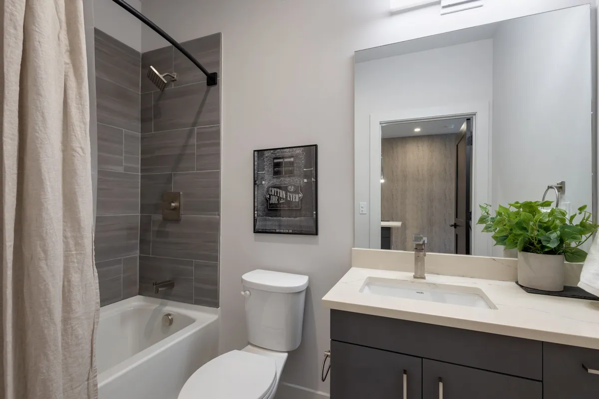 This bathroom showcases a serene environment with a bathtub, sink, mirror, framed artwork, and a plant. Inviting and spa-like, the space is designed for self-care and relaxation after a long day.