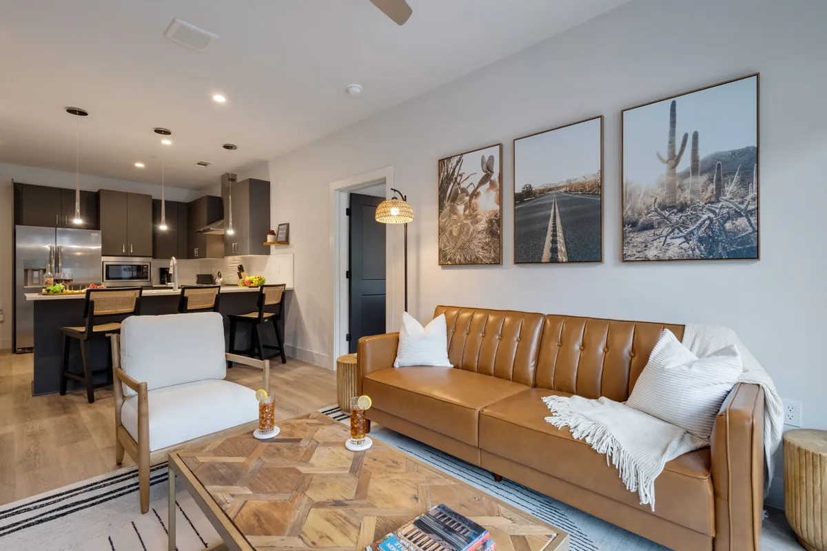 The image showcases a spacious, stylish living area featuring a plush leather sofa, striking modern artwork on the wall, and a sleek kitchen island—perfectly blending comfort and sophistication. The layout invites both relaxation and social gatherings, with ample room for entertaining, sharing meals, or unwinding after a day in Nashville.