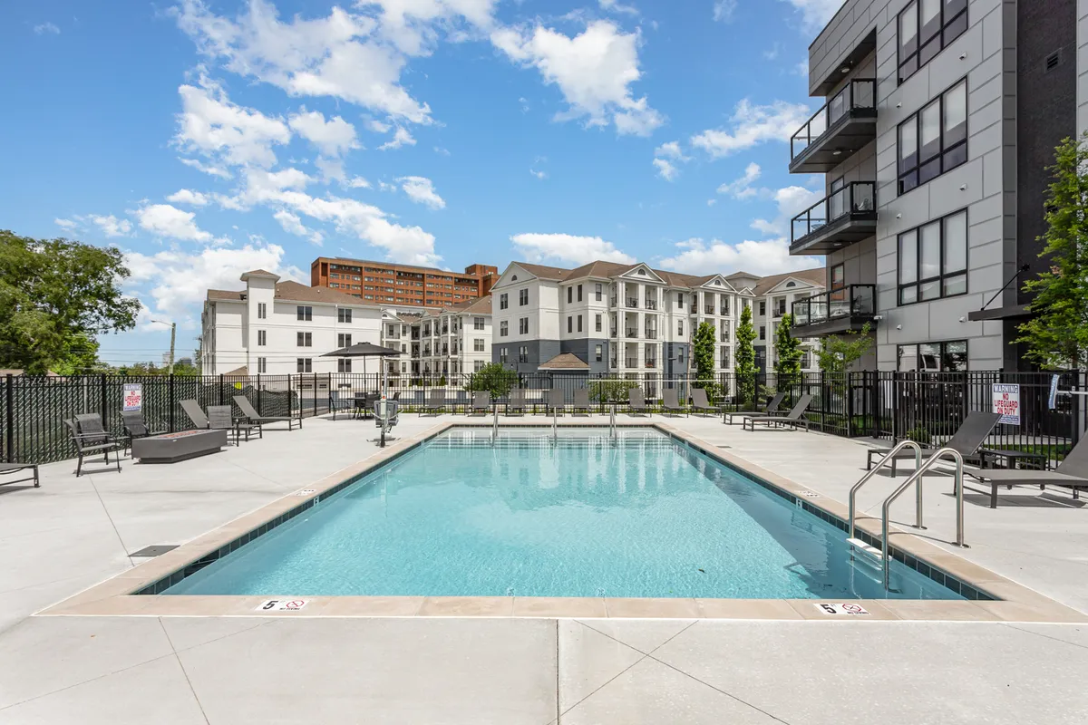 A view of a swimming pool lined with lounge chairs and framed by the surrounding modern building. The pool area feels welcoming, perfect for sunbathing, swimming, or spending time with family and friends.
