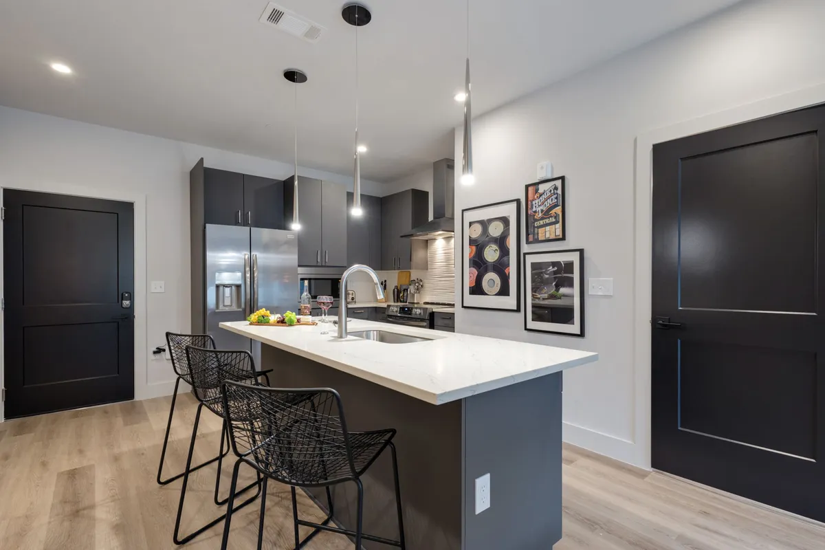 A welcoming kitchen scene centered on a large island with bar stools, surrounded by modern appliances and colorful wall art. The island invites guests to gather, while the open layout suggests ample space for group meal prep and entertaining.